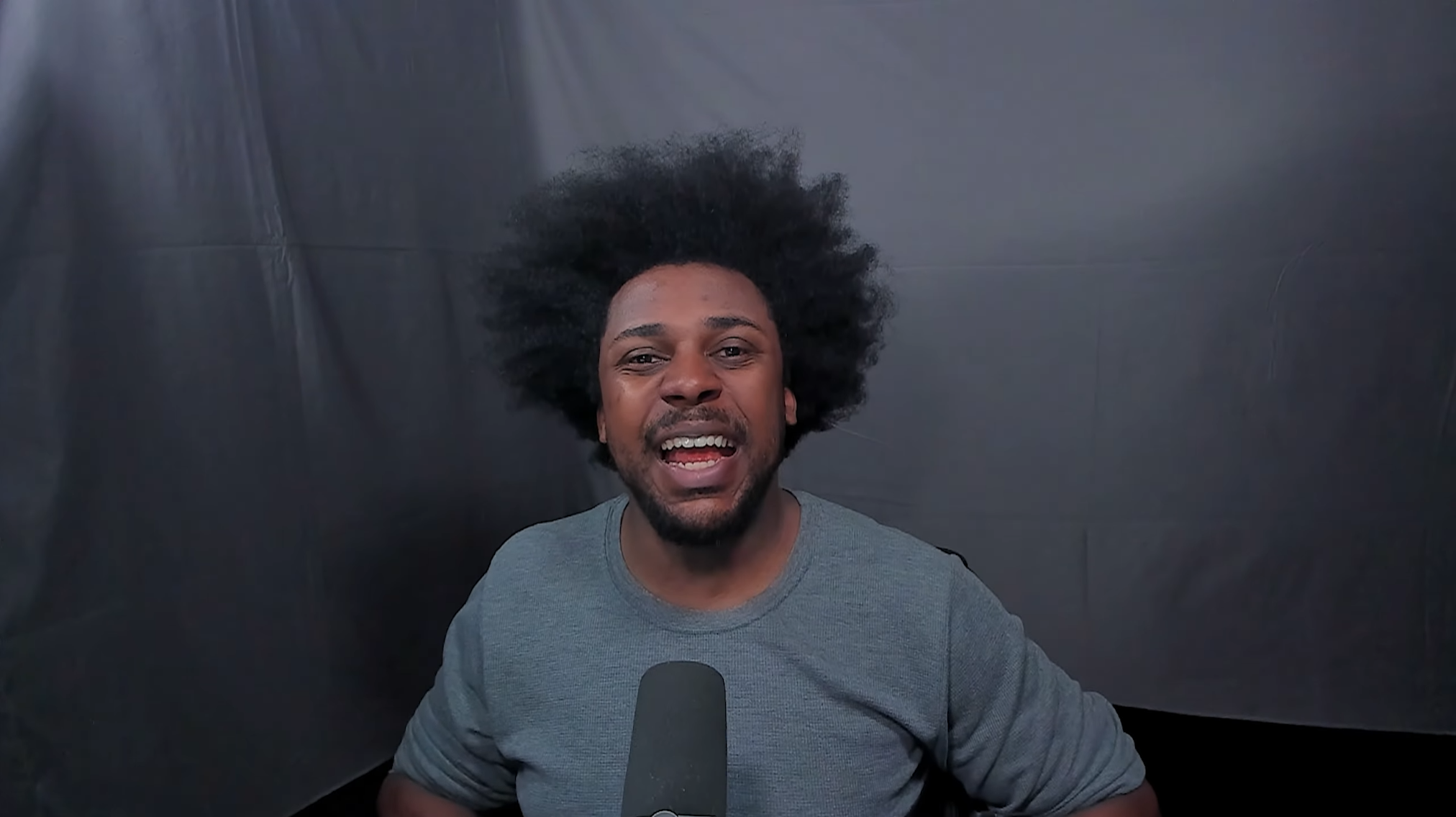 Liln at a mic in a stream setup, dark backdrop.